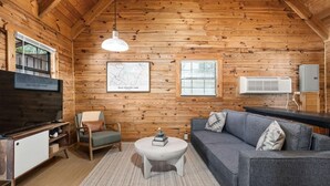 A cozy cabin interior with a wooden ceiling, a map on the wall, a sofa, a coffee table, and a TV. - Eagle's Perch Cabin 13 with Loft - One bed in loft, sleeper sofa and full kitchen (Allons)