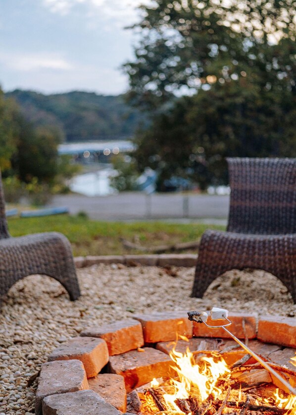 A fire pit with logs and a marshmallow roasting stick, surrounded by gravel. - Eagle's Perch Cabin 13 with Loft - One bed in loft, sleeper sofa and full kitchen (Allons)