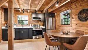 A modern kitchen with wooden walls, stainless steel appliances, and a round dining table with leather chairs. - Eagle's Perch Cabin 13 with Loft - One bed in loft, sleeper sofa and full kitchen (Allons)
