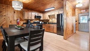 A modern kitchen with wooden cabinets, a dining table, and a black refrigerator. - 10 Person Golden Cedar Lodge 16 - 2 Floors and a 3rd floor loft, entertainment room, full kitchen (Allons)