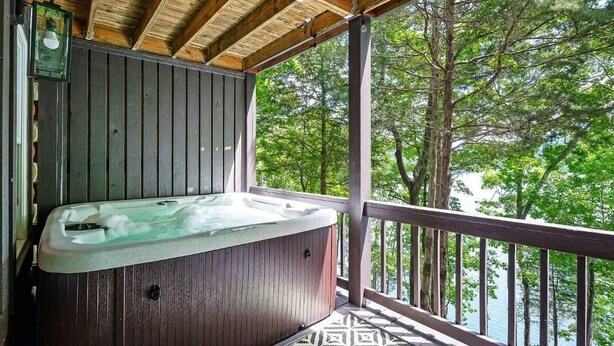 A wooden deck with a hot tub, surrounded by trees and overlooking a body of water. - 10 Person Golden Cedar Lodge 16 - 2 Floors and a 3rd floor loft, entertainment room, full kitchen (Allons)