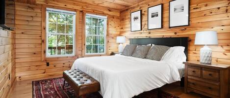 Un dormitorio con paneles de madera, una cama, un banco, mesitas de noche y cuadros en la pared.