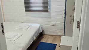 Una habitación con una cama, una alfombra azul, una ventana con persianas y una puerta.