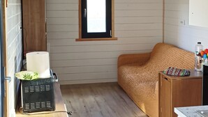 Habitación pequeña con suelo de madera, un ventanal, un sofá, una mesa, aire acondicionado montado en la pared y un extintor.