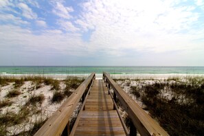 A wooden boardwalk leading to a beach with sand and sparse vegetation.