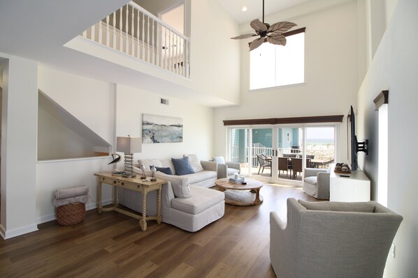 A spacious living room with a high ceiling, a staircase, and a balcony with a view.