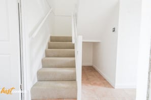 A staircase with beige carpeted steps leading to a landing with a white shelf. - Livingston 4 Bed + Car Space (West Lothian)