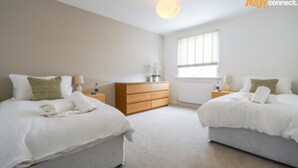 Een hotelkamer met twee bedden, een houten dressoir, een radiator en een raam met zonwering.