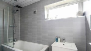 Een moderne badkamer met een douche in een glazen cabine, een vrijstaand bad en een wastafel met een raam erboven.