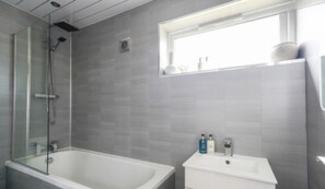 Ein modernes Badezimmer mit einer gläsernen Duschkabine, einer freistehenden Badewanne und einem Waschtisch mit Fenster darüber.