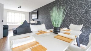 Een moderne eetruimte met een witte tafel, houten placemats en een potplant.
