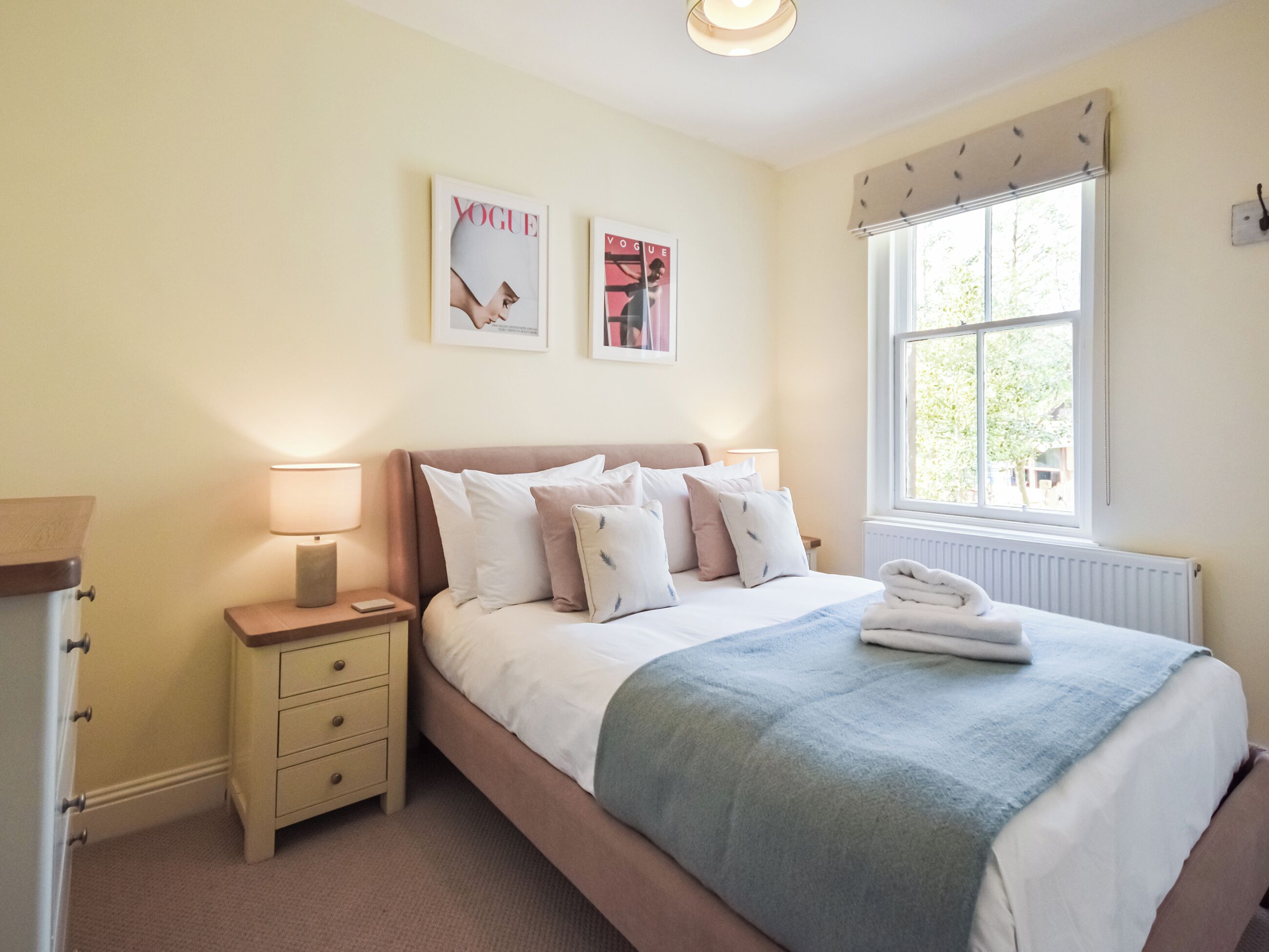A bedroom with a bed, bedside tables, lamps, a window with a view, and two framed pictures on the wall.