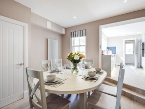 A dining area with a round table set for four, white chairs, and a vase with flowers.