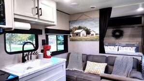 Een compact RV-interieur met een kitchenette, een bank met gestreepte kussens en een muurschildering van een landschap.