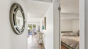 A hallway leading to a bedroom with a bed, a dresser, and a mirror. - Hibiscus Resort Condo with Pool View (St. Augustine)