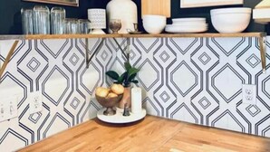 A kitchen counter with a geometric patterned backsplash, a vase with green foliage, and various kitchen items. - The 'Posh Pickle'- Chic & Unique

 (louisville)