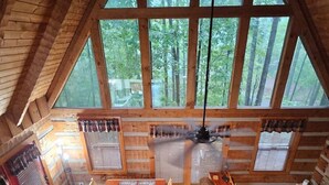 Eine Holzhütte mit Essbereich, Kamin und großen Fenstern mit Blick auf den Wald.