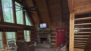 Ein Blockhaus-Interieur mit Kamin aus Stein, Holzmöbeln und einem darüber hängenden Fernseher.