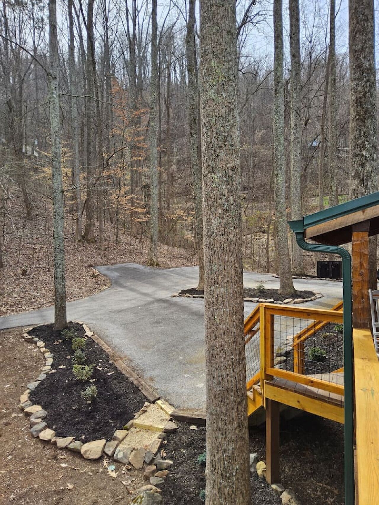 A forested area with a paved path, a wooden deck, and a stone border.
