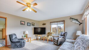 A living room with a ceiling fan, a television, and a fish mounted on the wall. - Michigan Manistee River Cabin ~ 1 Mi to Downtown (Manistee)