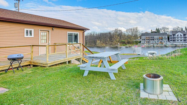 A lakeside cabin with a deck, picnic table, grill, and a metal fire pit. - Michigan Manistee River Cabin ~ 1 Mi to Downtown (Manistee)