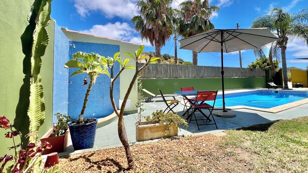 A pool area with a blue tiled wall, a small palm tree, and a patio with a table and chairs. - Countryside Haven, Between Lagos and Praia da Luz & Along the Ecovia Bike Trail (Lagos)
