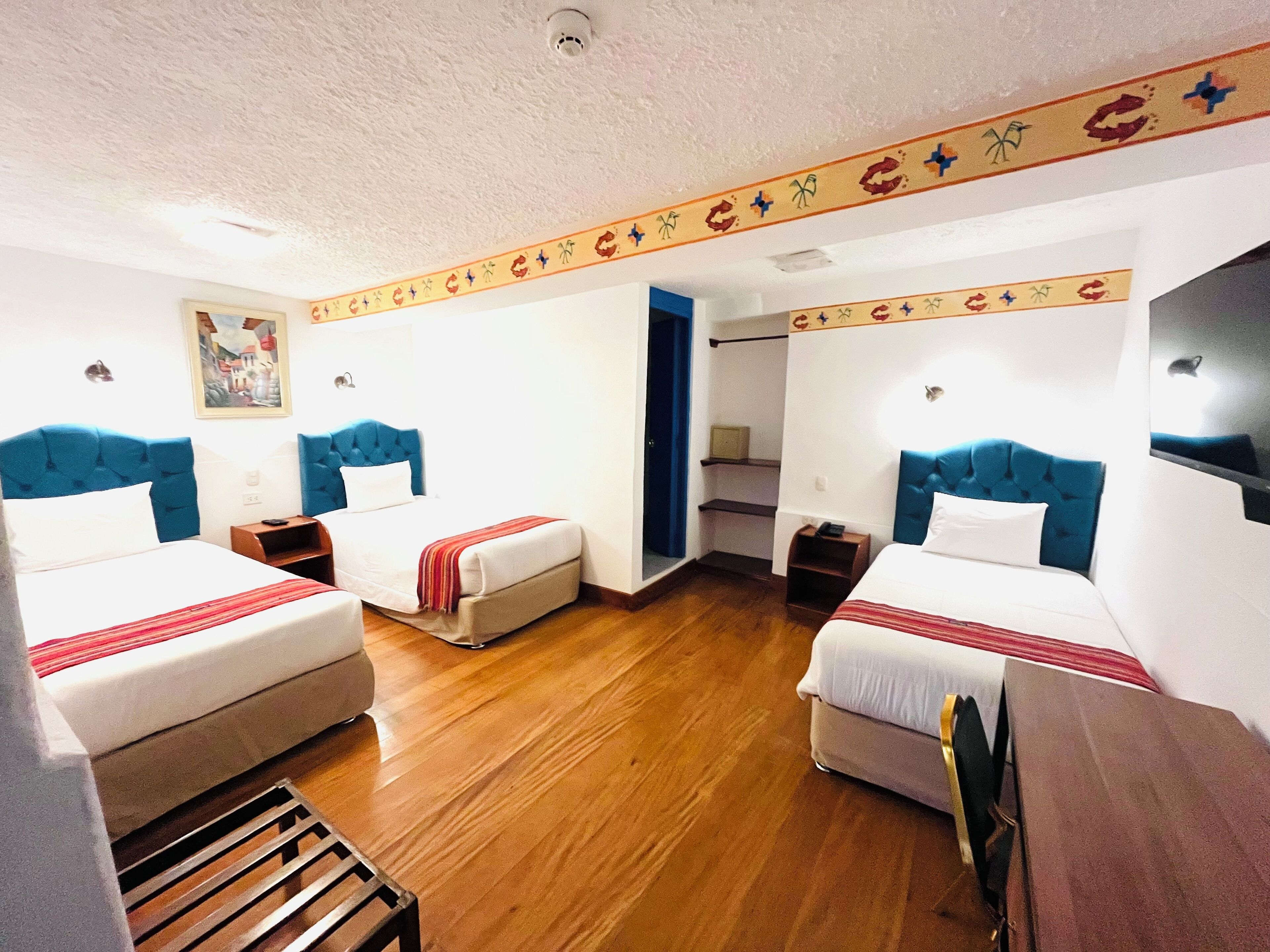 A hotel room with two beds, wooden flooring, and a decorative border along the ceiling.