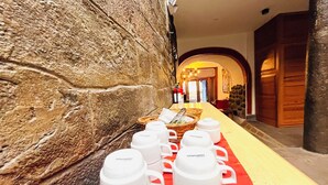 Un couloir d’hôtel avec une longue table dressée, ornée de tasses et de bols blancs de la marque Iichimatsu, des murs en pierre et une moquette rouge.