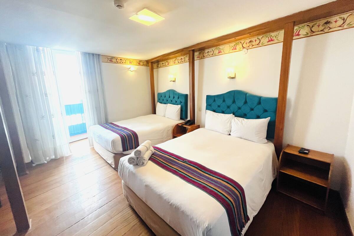 Une chambre d’hôtel avec deux lits, un plancher en bois, une couverture à rayures et une petite table d’appoint en bois.