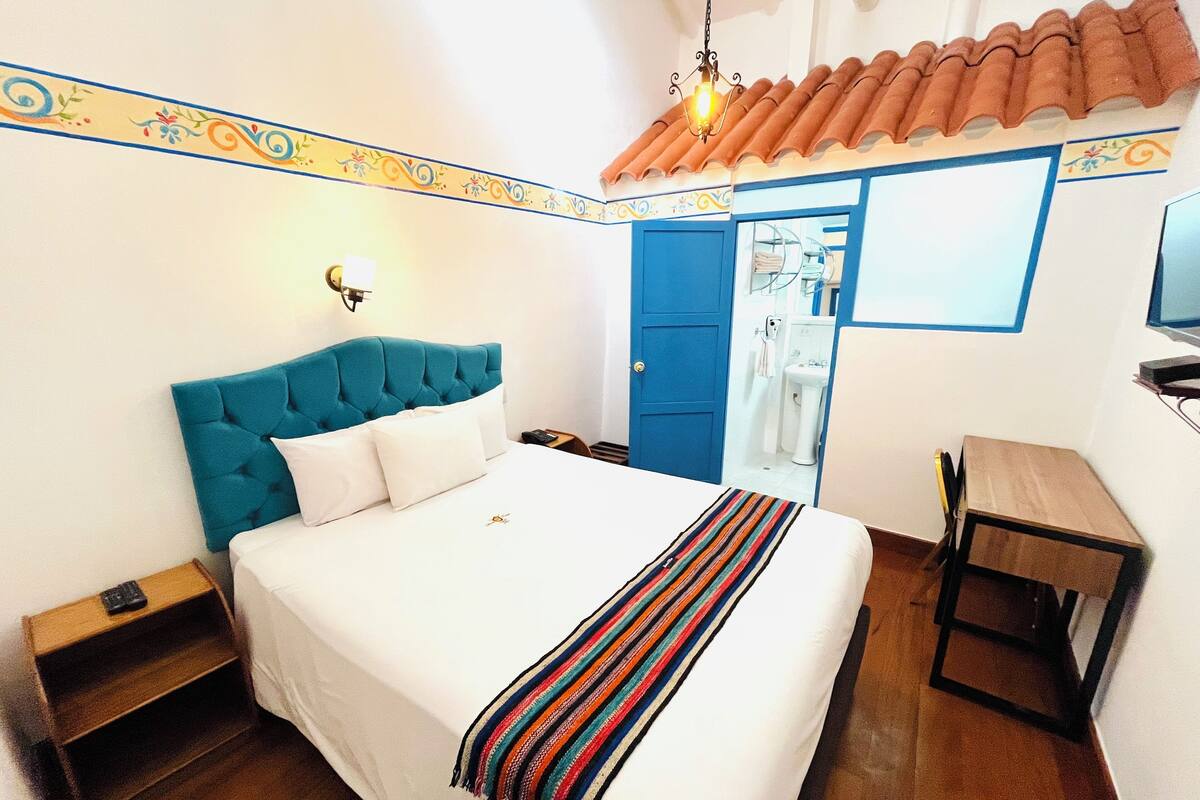 Une chambre à coucher avec un grand lit, une table de chevet, un bureau et une salle de bain visible à travers une porte ouverte.