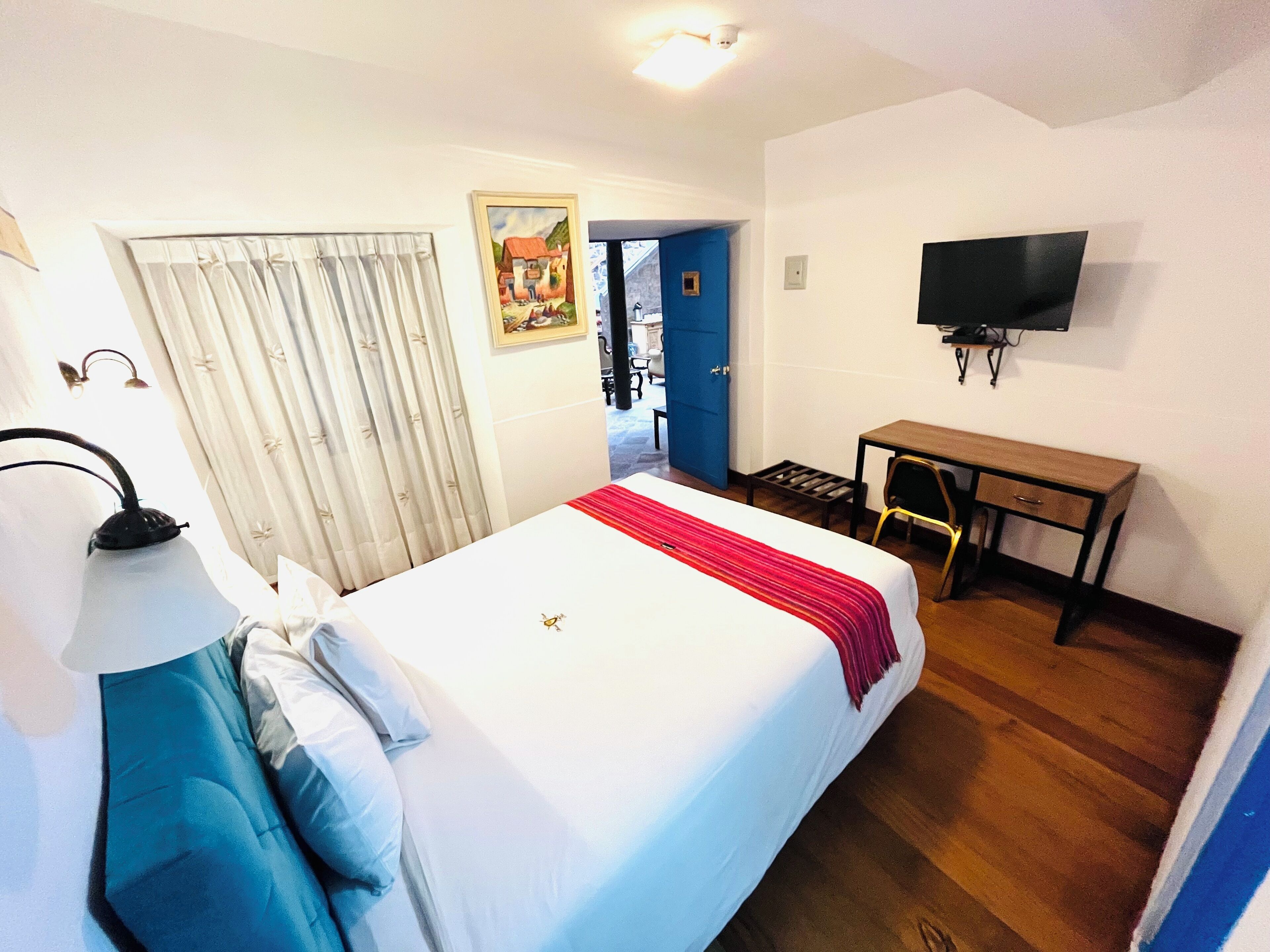 A hotel room with a bed, a desk, a television, and a door leading to another room.