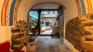 Un couloir avec un mur de pierre d’un côté et un canapé rouge de l’autre, qui mène à un espace extérieur doté d’une porte bleue et d’un balcon.