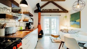 A modern kitchen with white cabinets, a wooden countertop, and a gas stove. There is a dining area with a white table and chairs, and a painting on the wall.