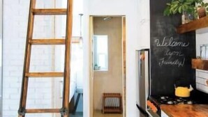 A kitchen with a wooden ladder, a chalkboard with "Welcome" written on it, and a view into another room.