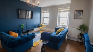 Un salon moderne avec des canapés bleus, un téléviseur à écran plat et un lustre.