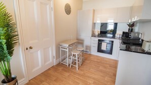 Une cuisine moderne avec des meubles blancs, un plancher en bois, un petit coin bar et une plante en pot.