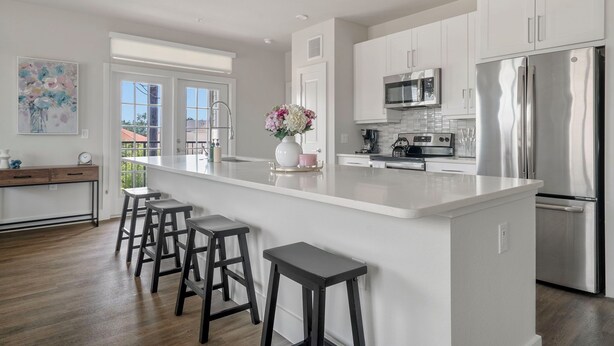 Cocina moderna con armarios blancos, electrodomésticos de acero inoxidable y una isla central con taburetes de bar.