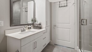 Un baño moderno con tocador blanco, un espejo grande y una cabina de ducha de vidrio.