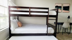 Una cama individual superpuesta con ropa de cama blanca, un escritorio con silla y dos cuadros en la pared.