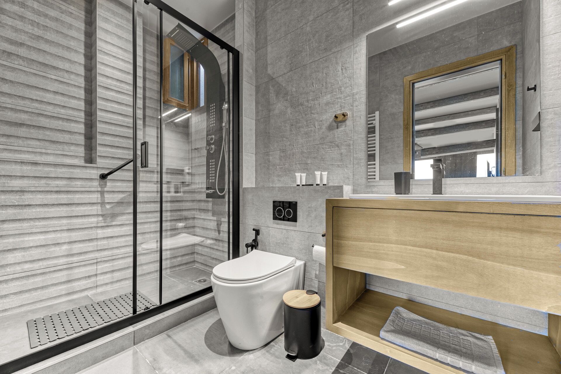 A modern bathroom with a glass shower enclosure, a toilet, a sink with a wooden vanity, and a mirror.