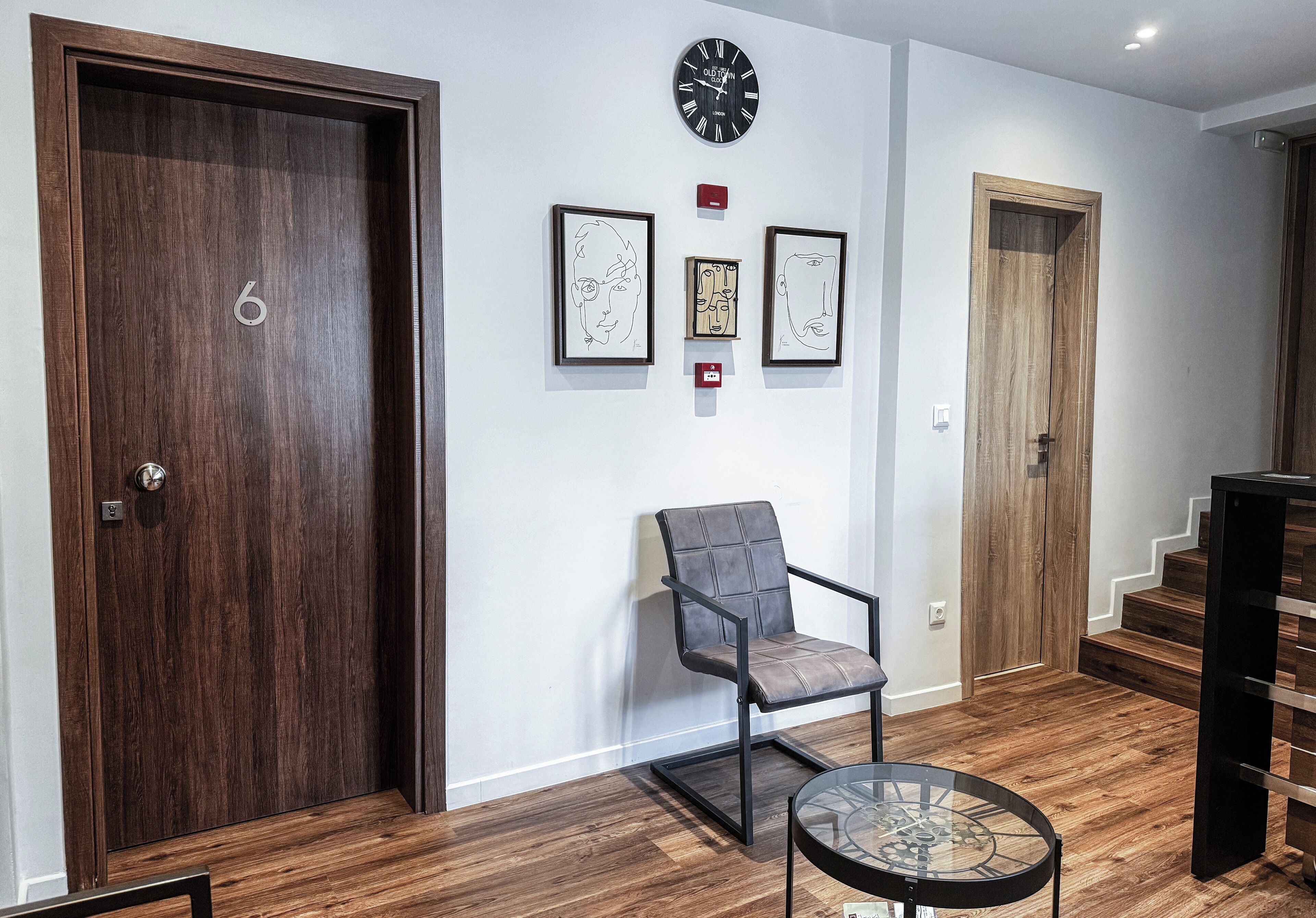 A modern interior with a wooden floor, a glass table, a cushioned chair, and framed artwork on the wall.