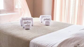 A hotel room with a neatly made bed, a window with sheer curtains, and several towels with the brand name "Komody" on them.