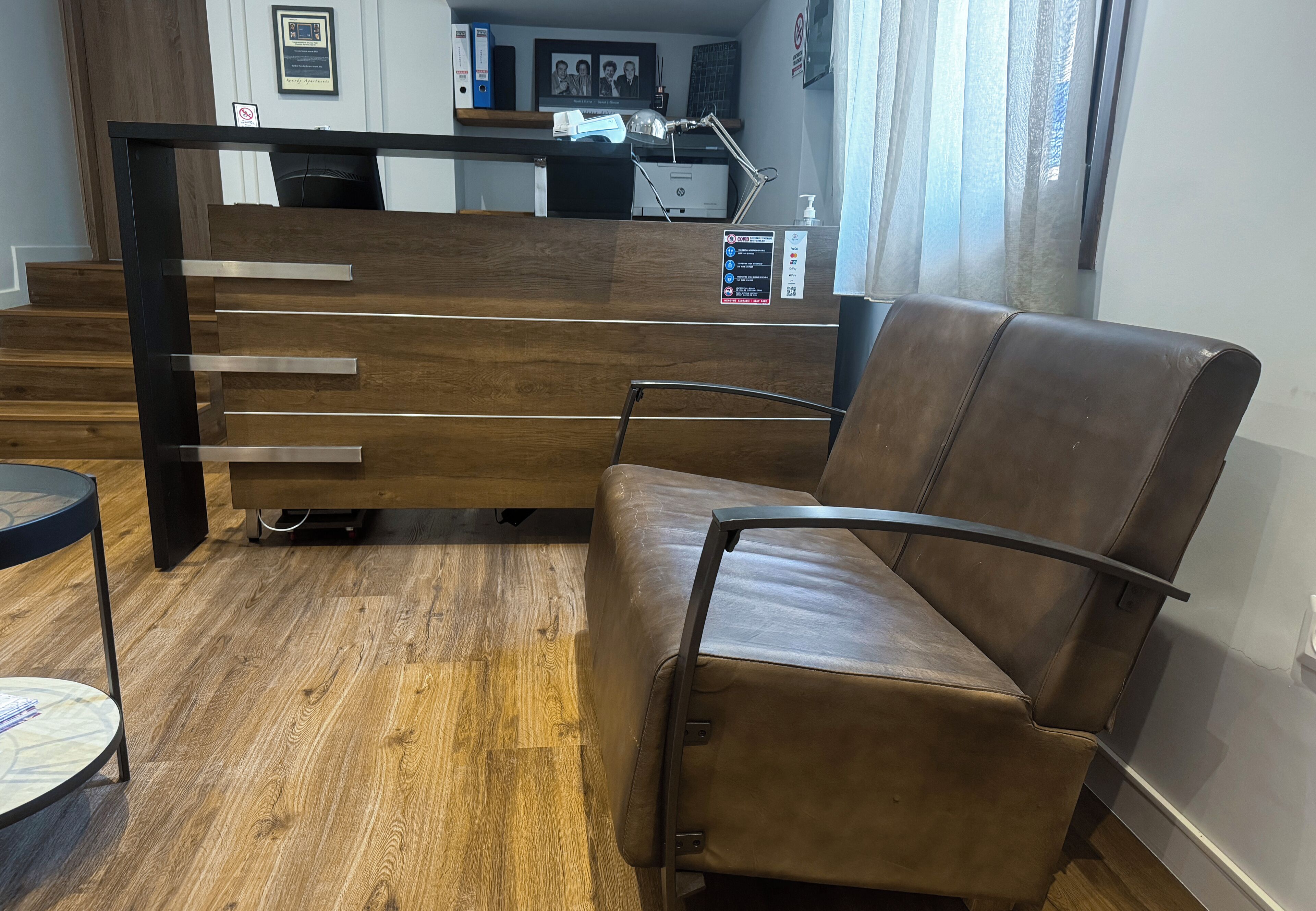 A waiting area with a brown leather chair, a wooden reception desk, and a wooden floor.