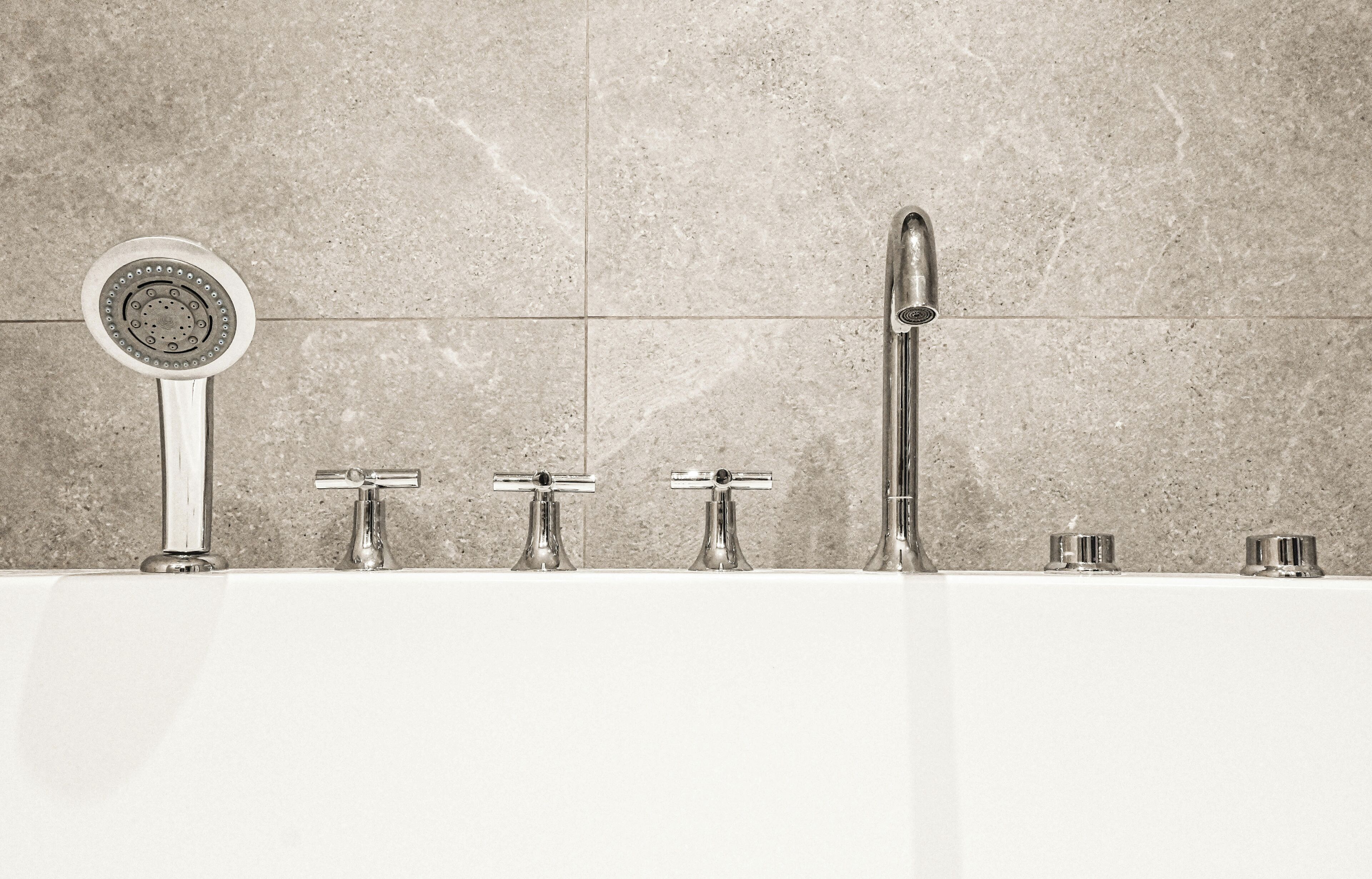 A bathroom with a bathtub, a handheld showerhead, and a wall-mounted faucet.