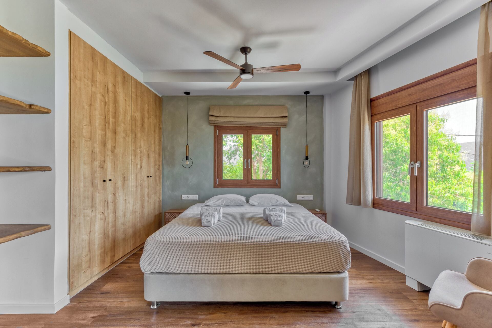 Un dormitorio con cama, armario de madera, ventilador de techo, ventana y radiador.