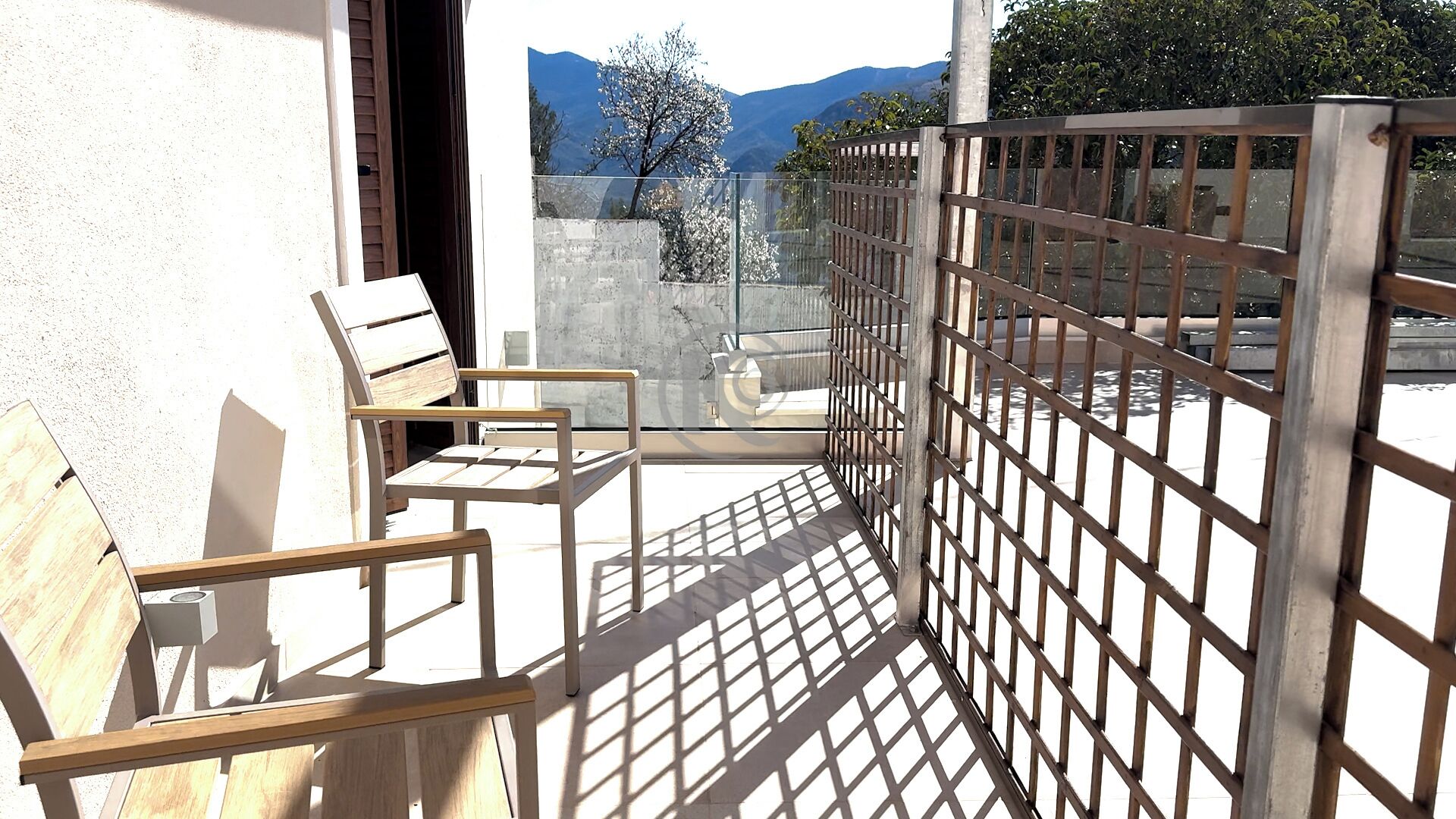 A balcony with a wooden chair, a metal fence, and a view of mountains and trees.