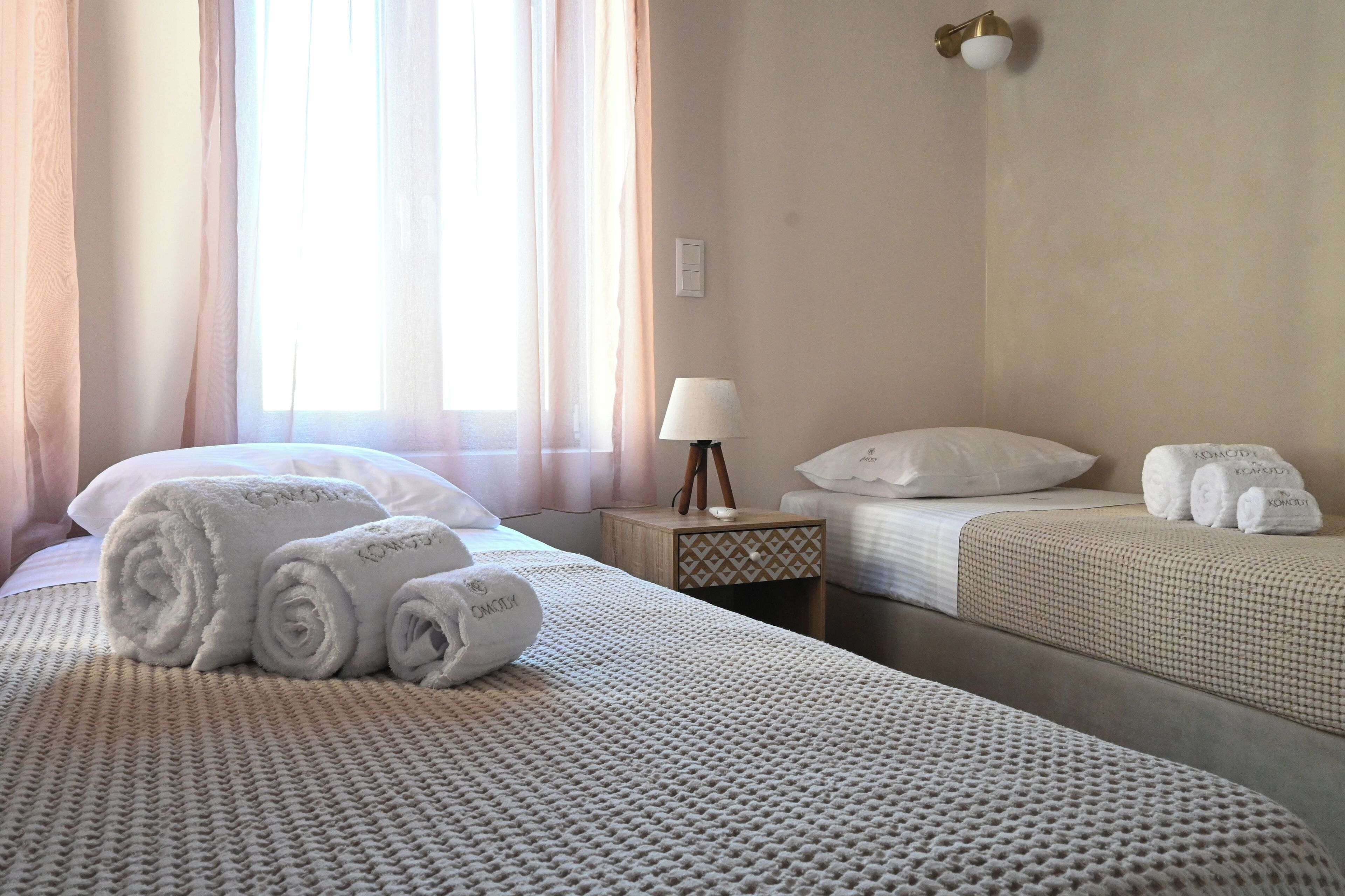 Habitación de hotel con dos camas, una mesita de noche con lámpara y toallas enrolladas sobre las camas.
