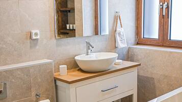 Un baño moderno con una bañera independiente, un espejo grande y un mueble lavamanos.