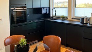 A modern kitchen with black cabinets, a built-in oven, and a window with a view of the outside. - Park View Apartment (Bremerhaven)