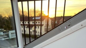 A balcony with a view of residential buildings and a sunset. - Park View Apartment (Bremerhaven)